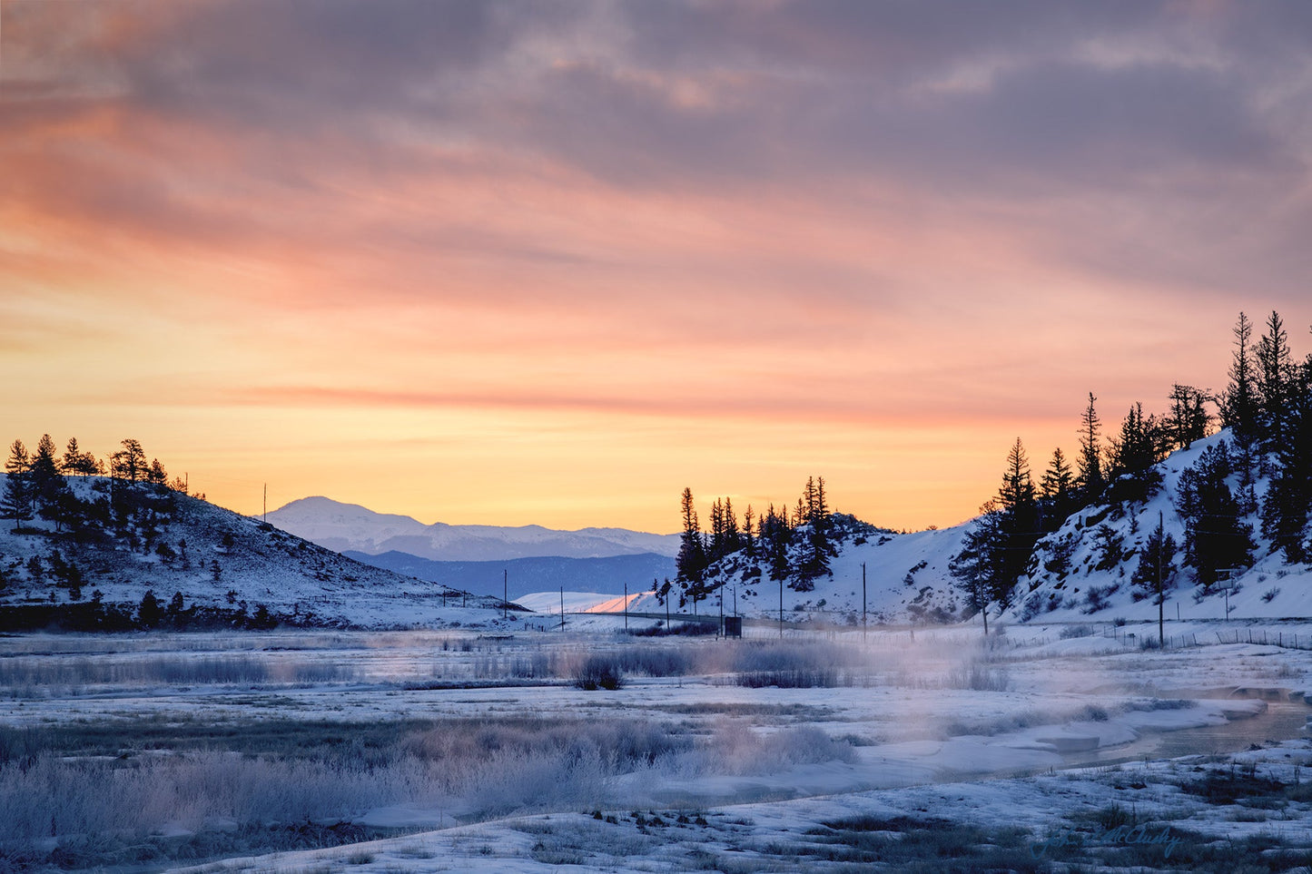 Mists rise from a thawing creek, glowing from an orange sherbet sunrise. Pikes Peak rises in the distance. Fine art landscape photography by McClusky Nature Photography.