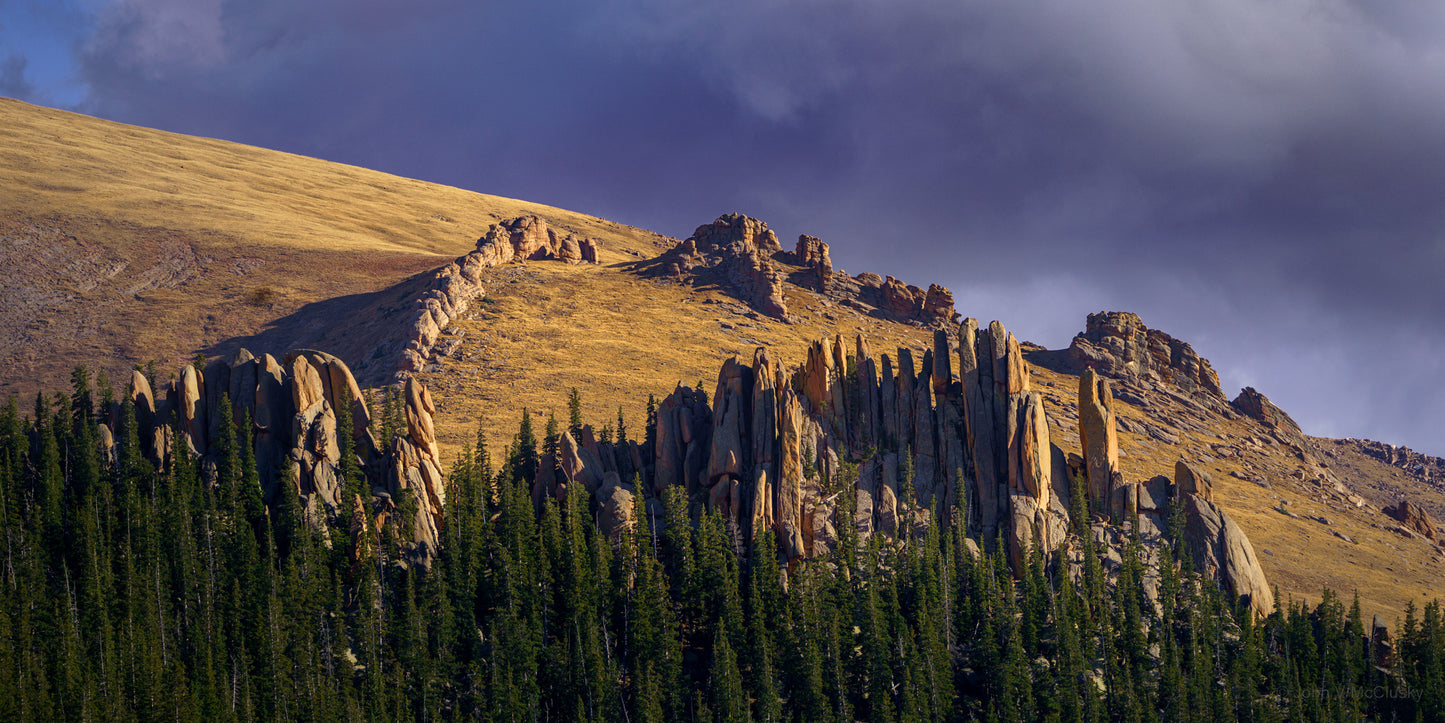 Granite dikes and pillars are lit by the sun above the Pikes Peak tree line with foreboding clouds in the background of this fine art print.