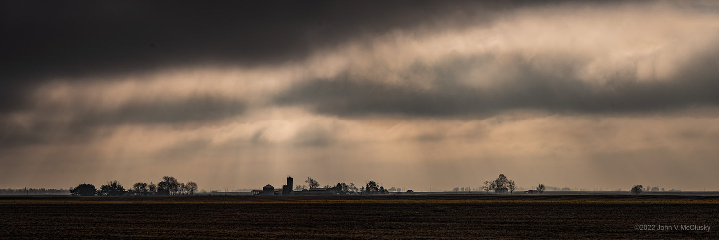 Dramatic clouds and god rays overlook distant homesteads on the Illinois plains. Landscape photography Print by McClusky Nature Photography.