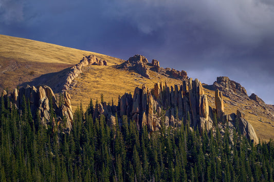 Granite dikes and pillars are lit by the sun above the Pikes Peak tree line with foreboding clouds in the background of this fine art print.