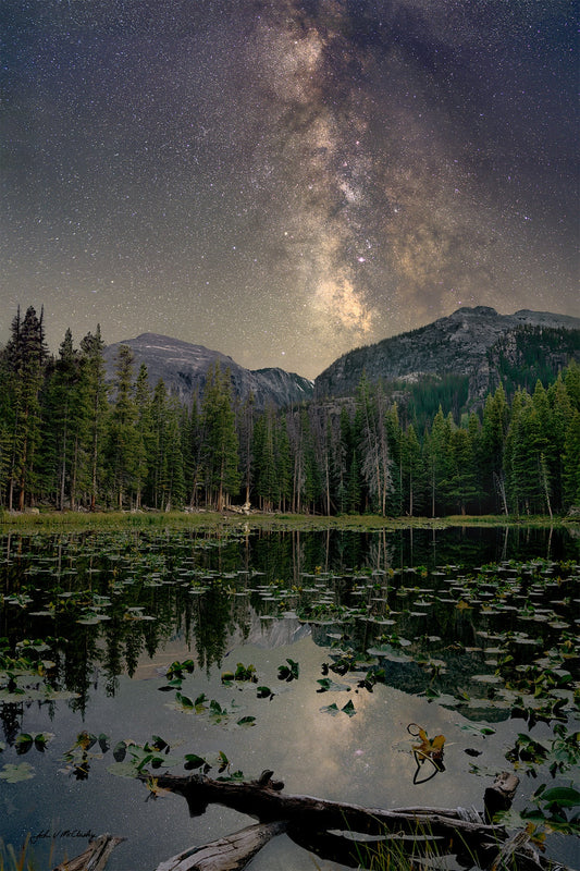 The Milky Way glows over Lilly Lake iin Rocky Mountain National Park with trees and mountains in the background
