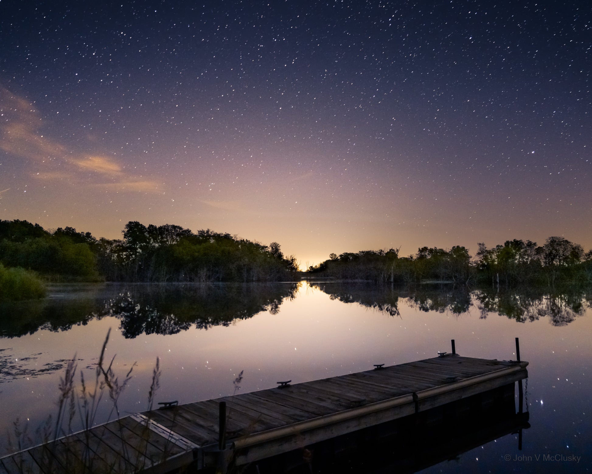 A fishing pier extends into Gridley Lake with the far shore and a starry sky reflected in the waters.  Fine Art Nature photography by McClusky Nature Photography.