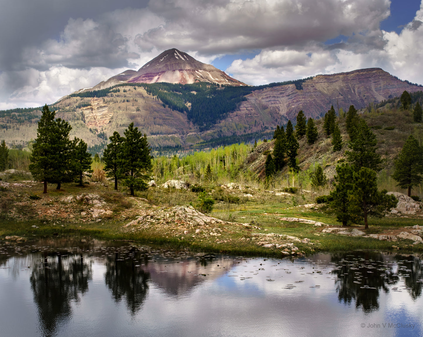 I was drawn to this image by the vibrant greens of the new aspen leaves and grasses contrasting with the maroon mountains. The soft reflection of the mountain and clouds and dark pines in the lake make this a favorite landscape photography image.